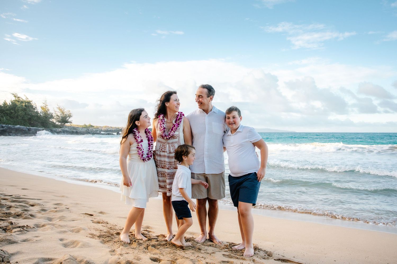 Family walking together and smiling on a tropical beach with palm trees and ocean waves.