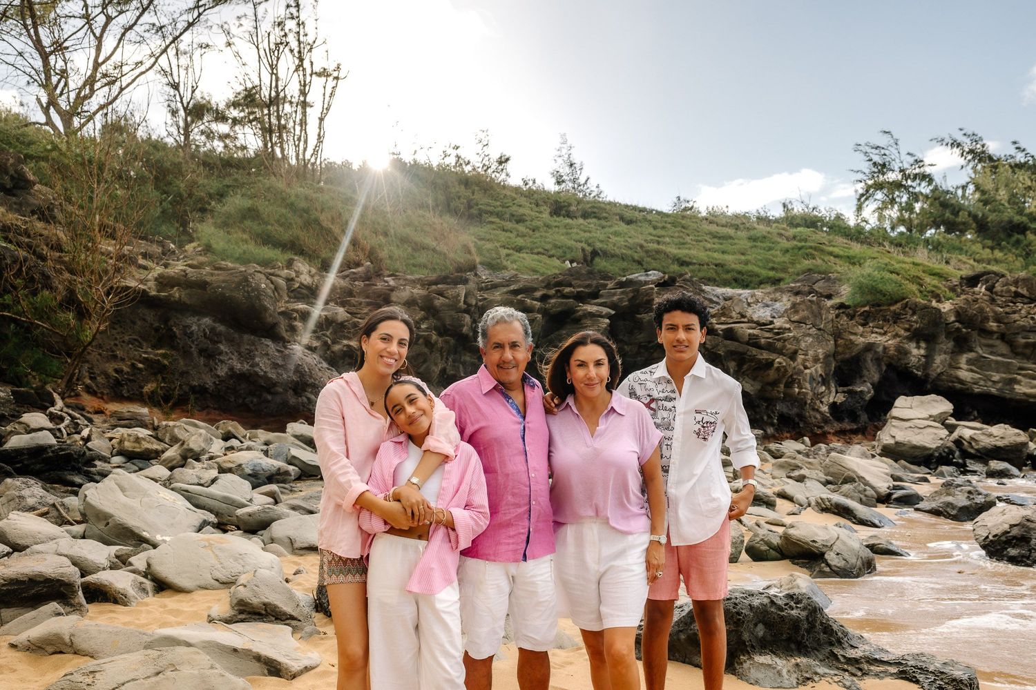 Family photo session on a rocky beach coastline with everyone in pink and white attire.