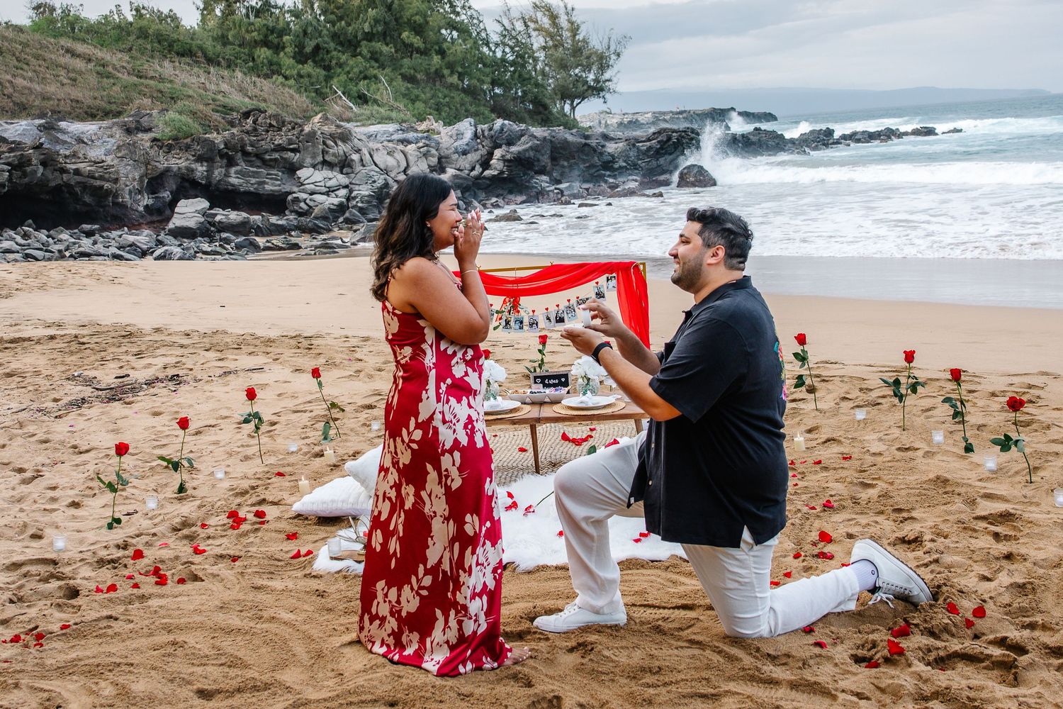 Beachside marriage proposal with red floral decorations and ocean view.