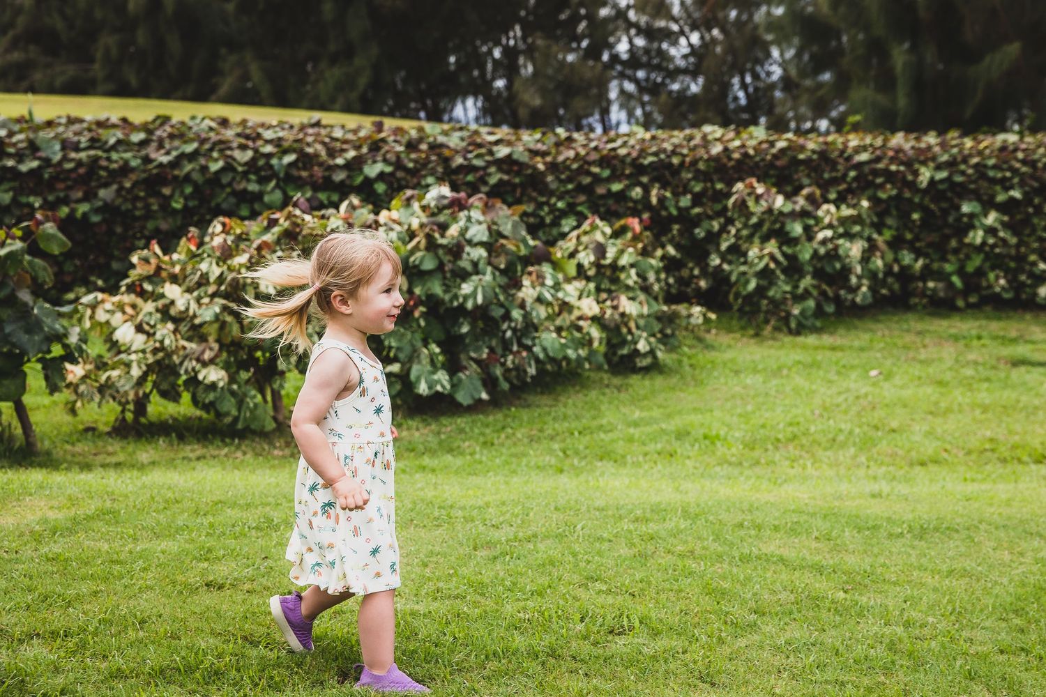 Young girl in a tropical print dress runs and plays on grass during a summer photo session.