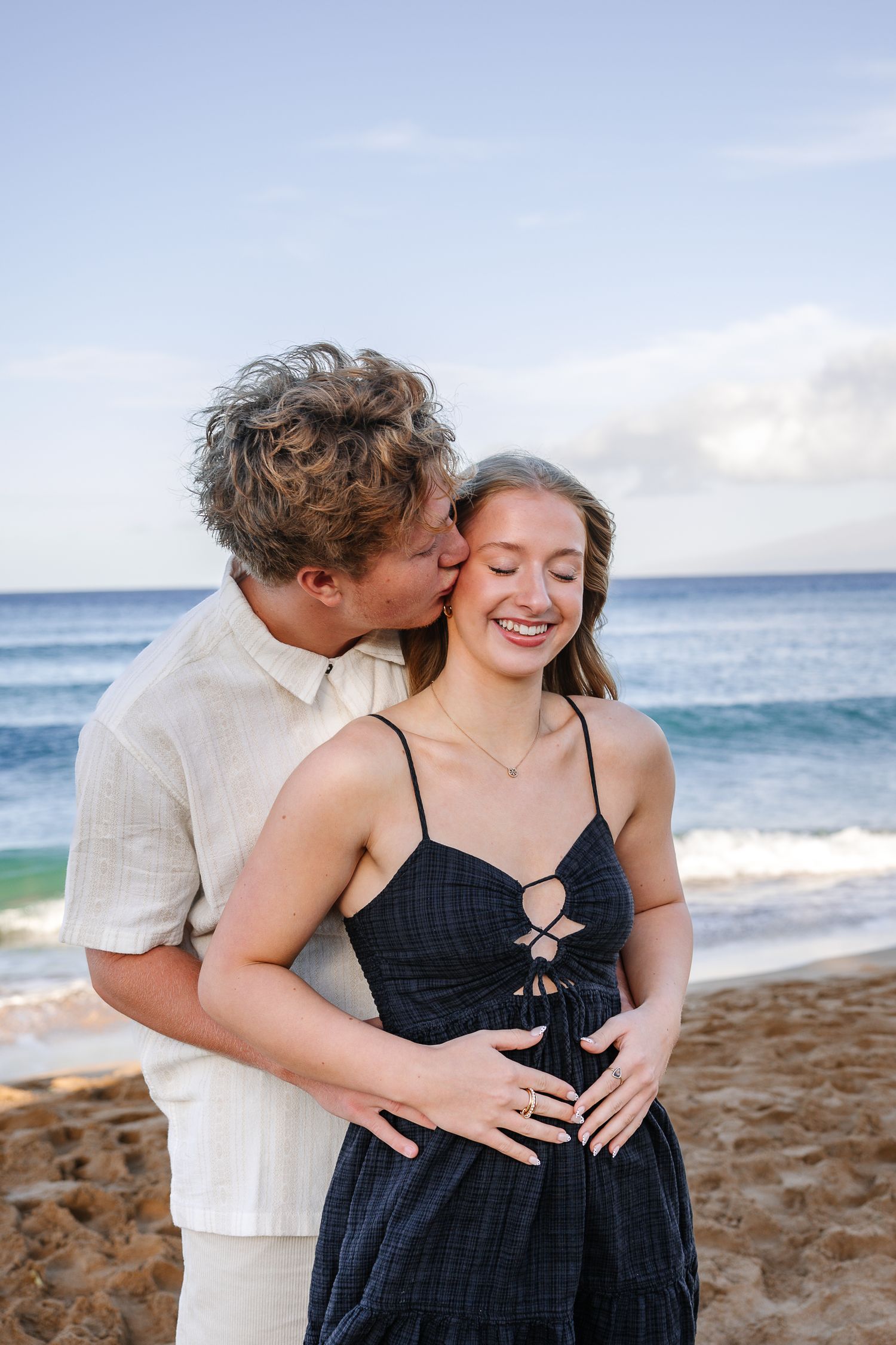 A couple shares intimate moments on a tropical beach with turquoise ocean waves in the background.