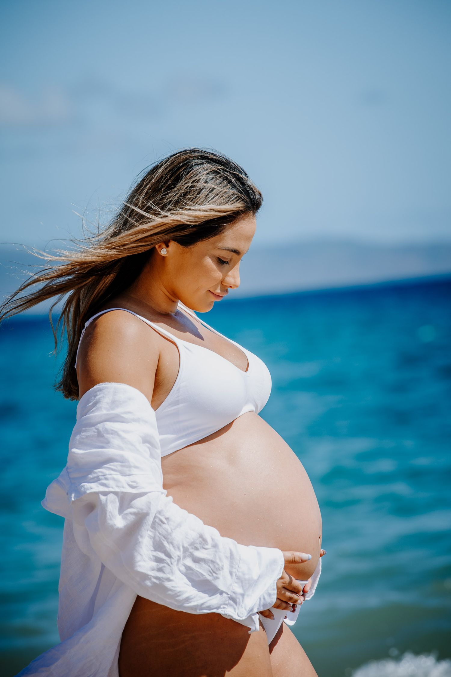 A side-view maternity portrait against vibrant blue ocean waters and sky.