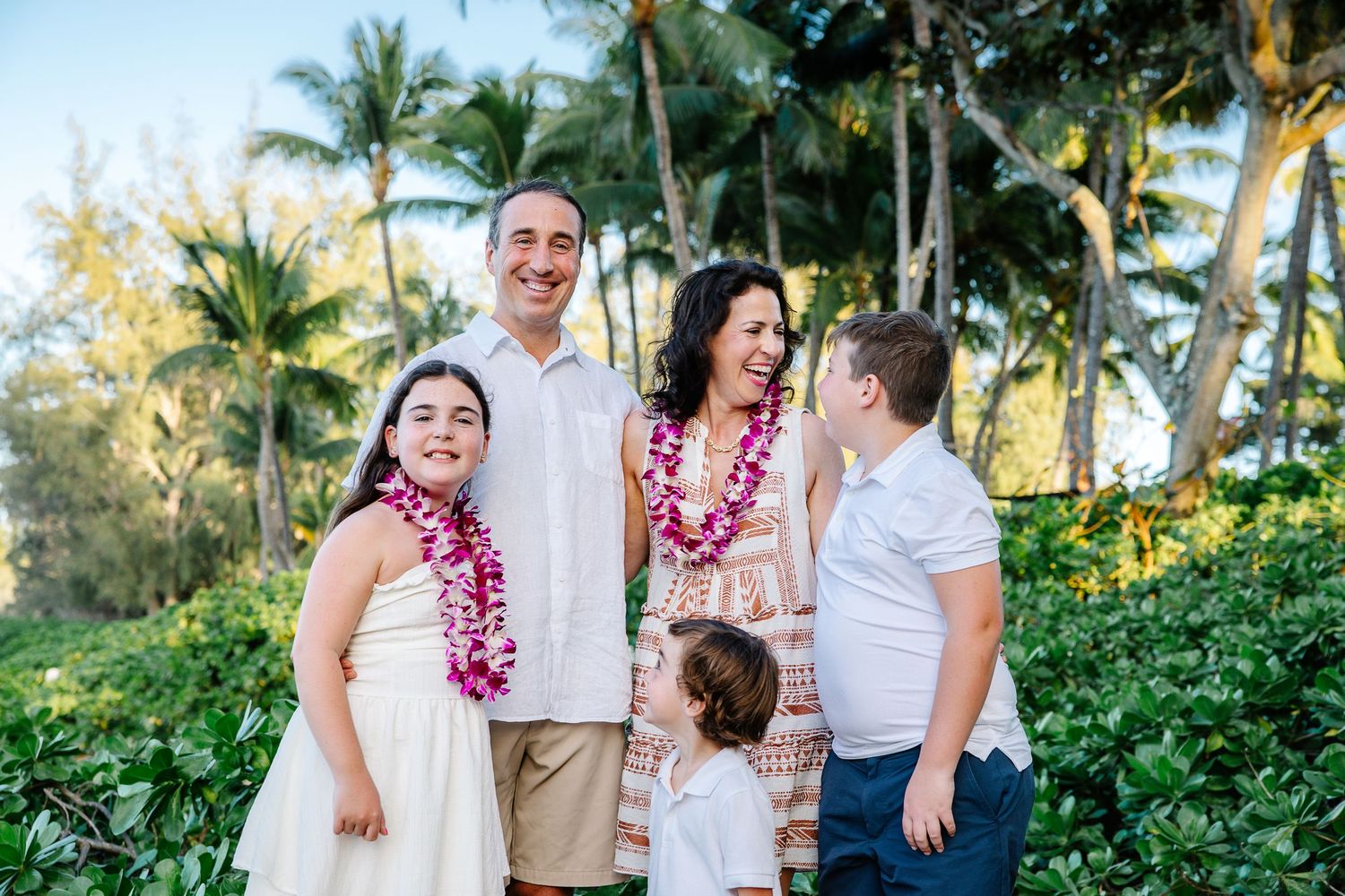 Tropical beach family photo session with palm trees and floral leis in Hawaii.