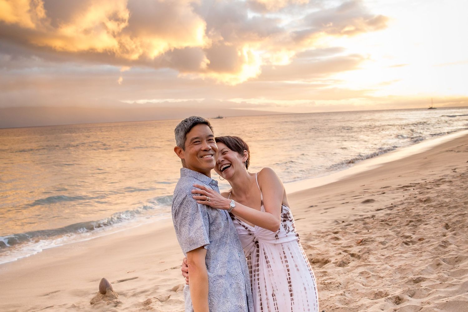 Couple embracing on sandy beach during vibrant sunset with waves in background.