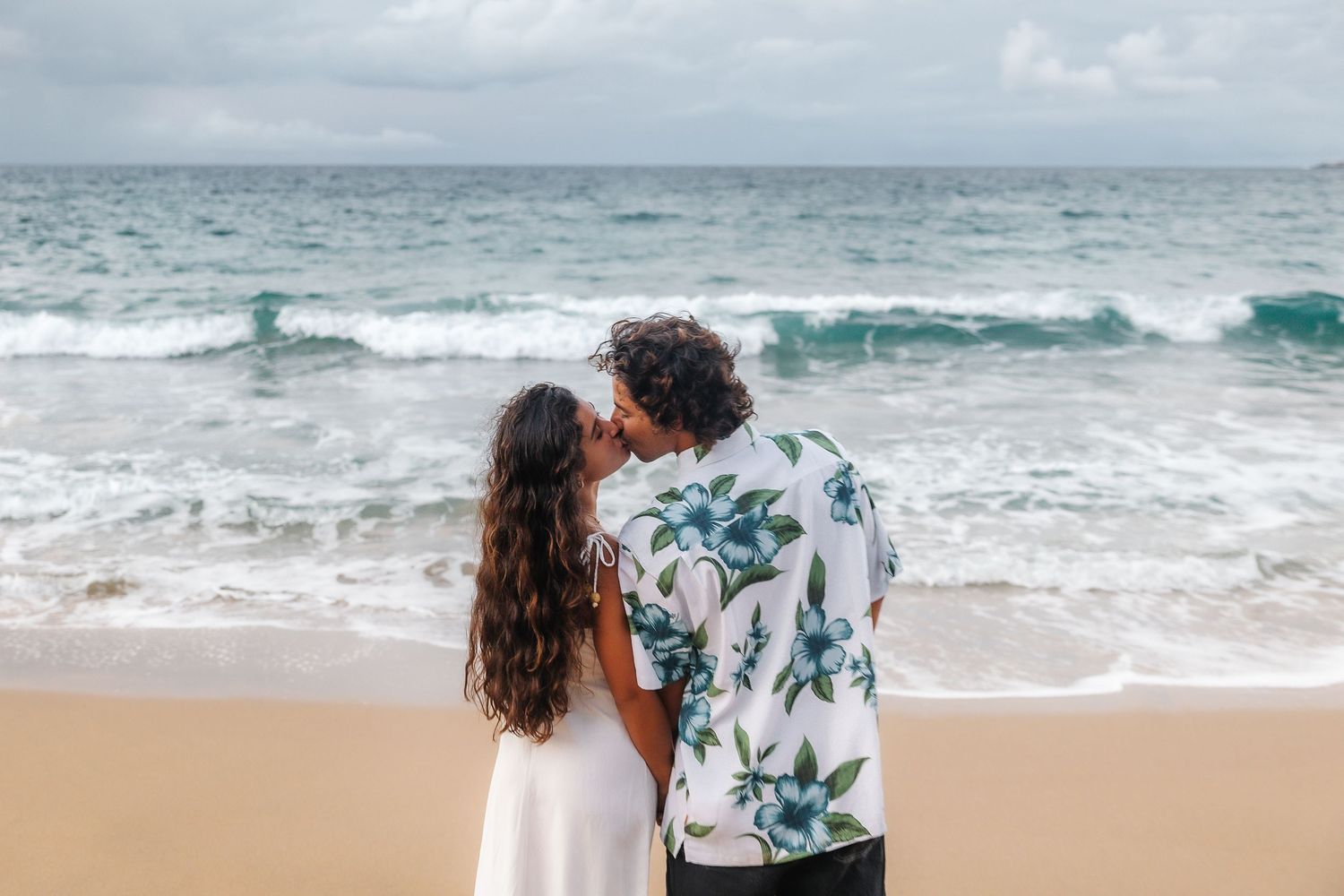 Romantic beach photoshoot with waves crashing and sandy shoreline in the background.