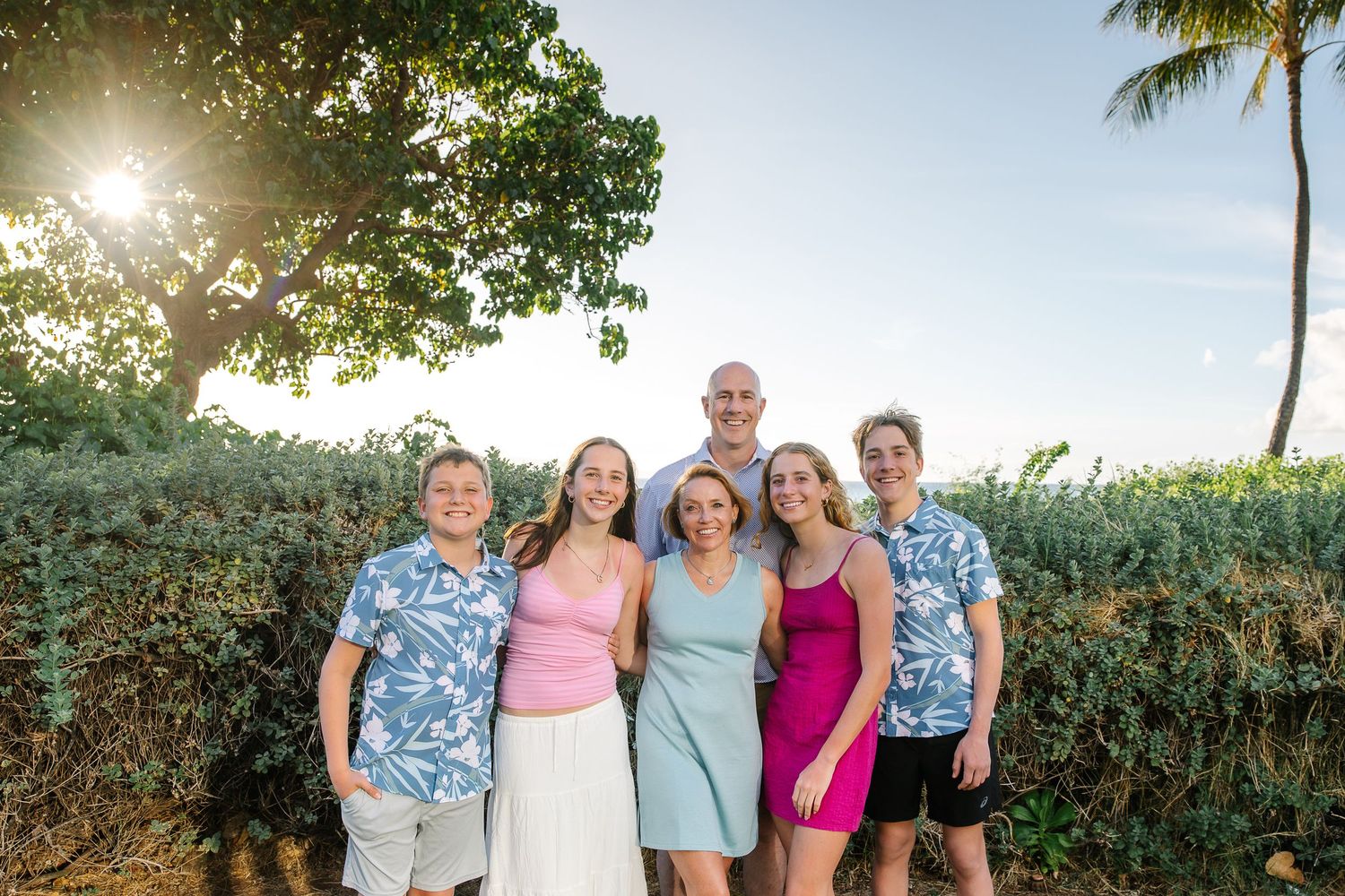 Family group poses for casual outdoor photos with tropical landscaping and palm trees.