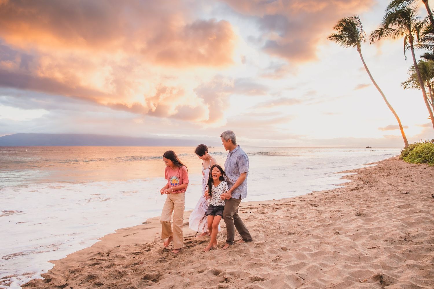 Family enjoying a beautiful sunset beach walk in Maui, Hawaii, with palm trees and colorful sky.