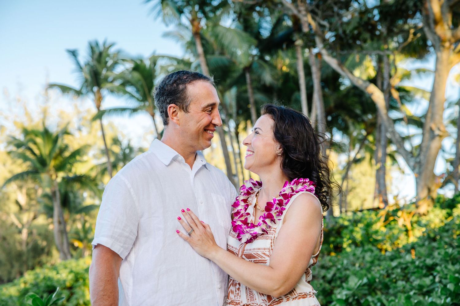 Romantic couple in tropical attire sharing a moment among palm trees on a Hawaiian beach.