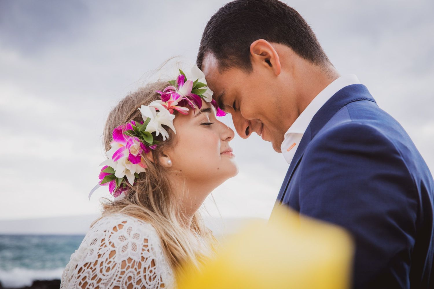 Couple in formal wear embracing near ocean with flower crown detail.