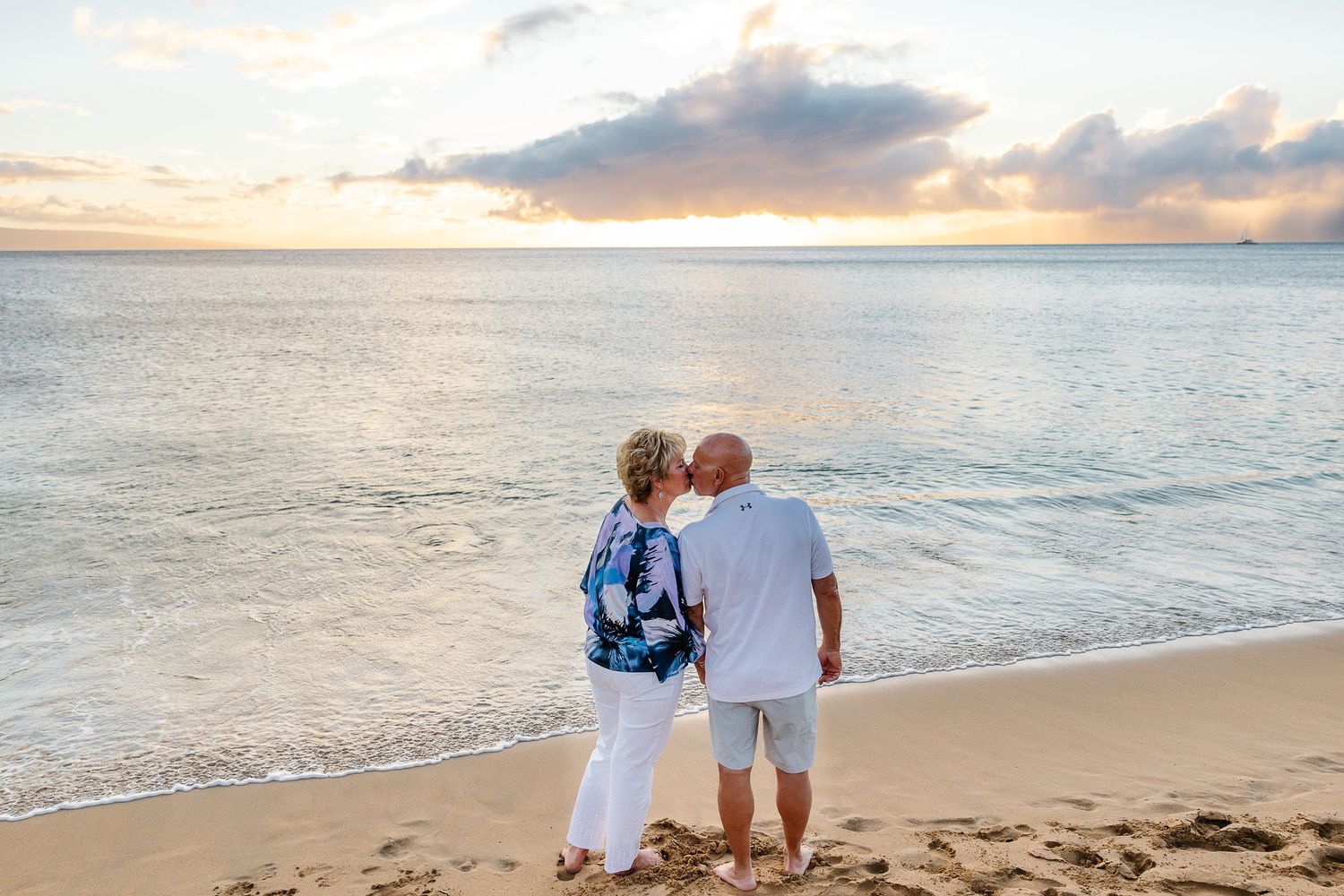 A couple stands together watching the sunset on a peaceful beach with gentle waves and golden light.