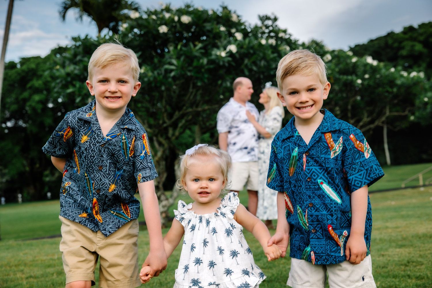 Children in coordinated blue and white outfits hold hands while walking on green grass.
