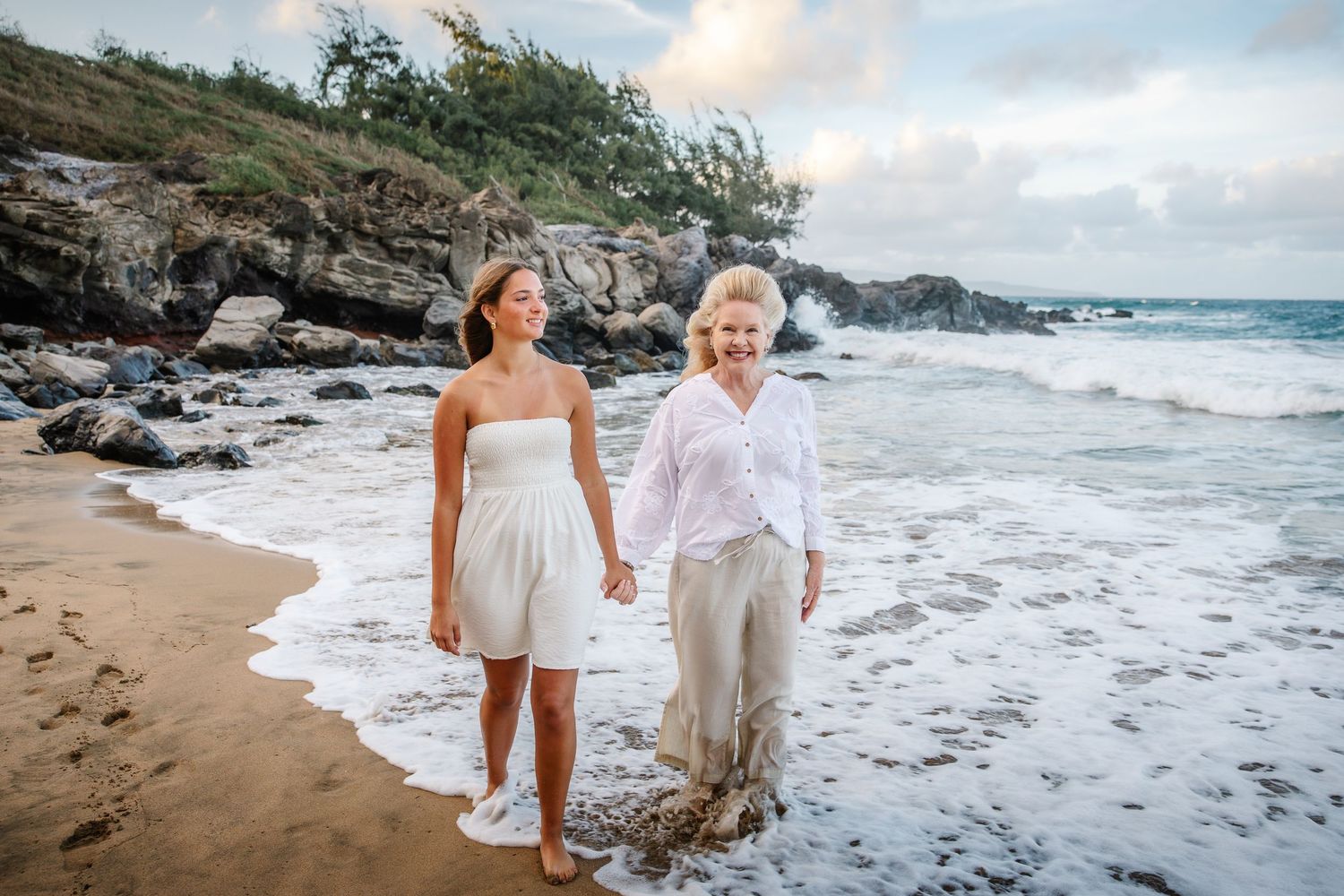 Two people walking along a scenic beach coastline at sunset in Hawaii.