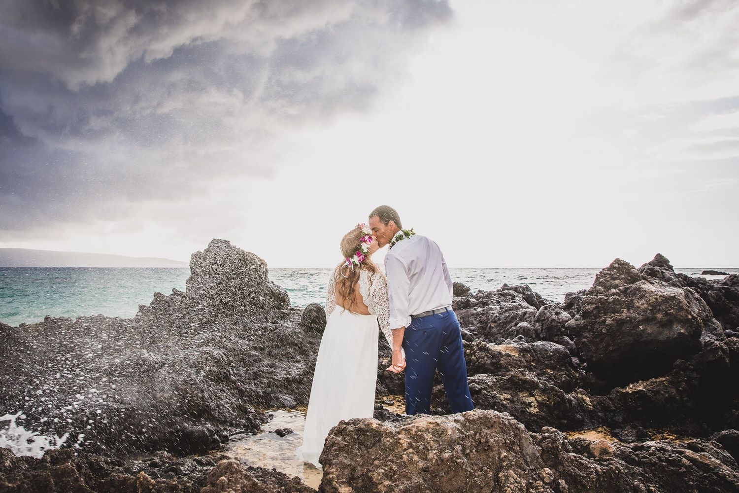 Dramatic coastal landscape with dark volcanic rocks against cloudy skies and ocean waves.
