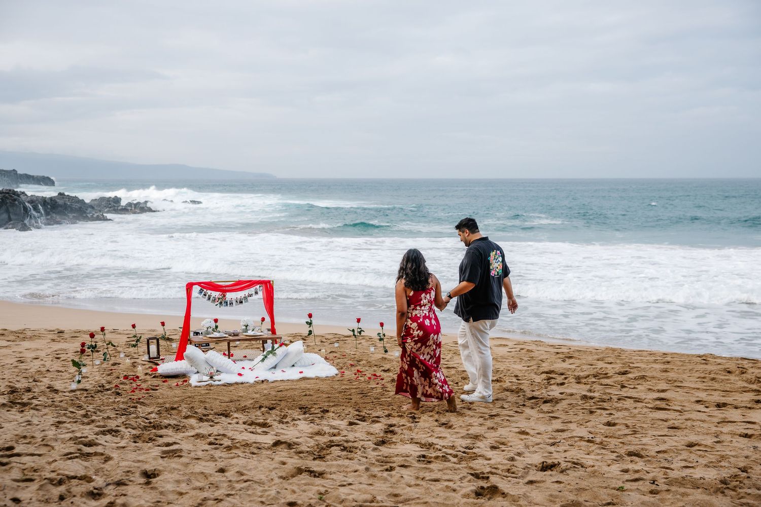 Beach proposal setting with red arch and ocean waves in background.
