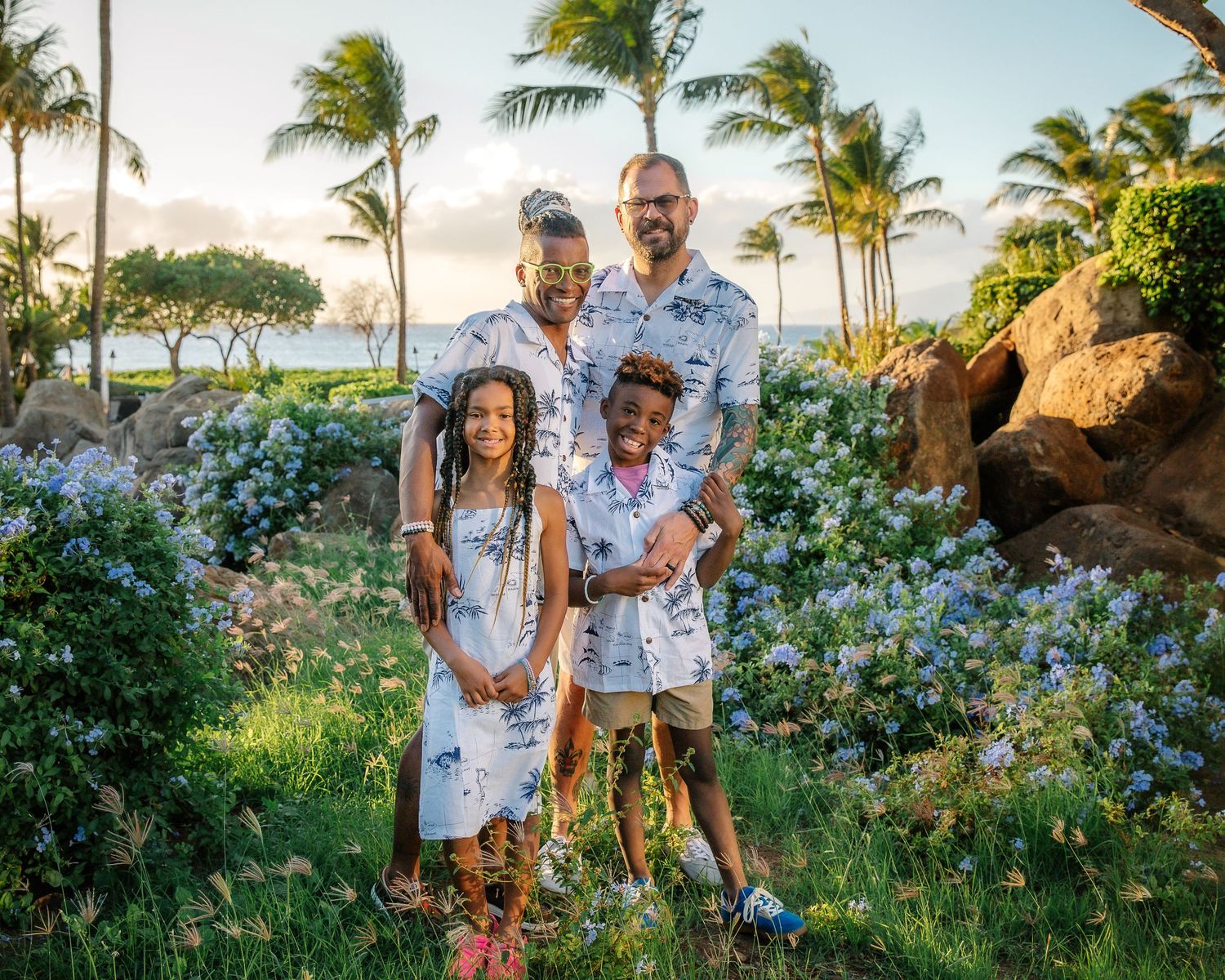 A family poses together in a tropical garden with palm trees and blue flowers at sunset in Hawaii.