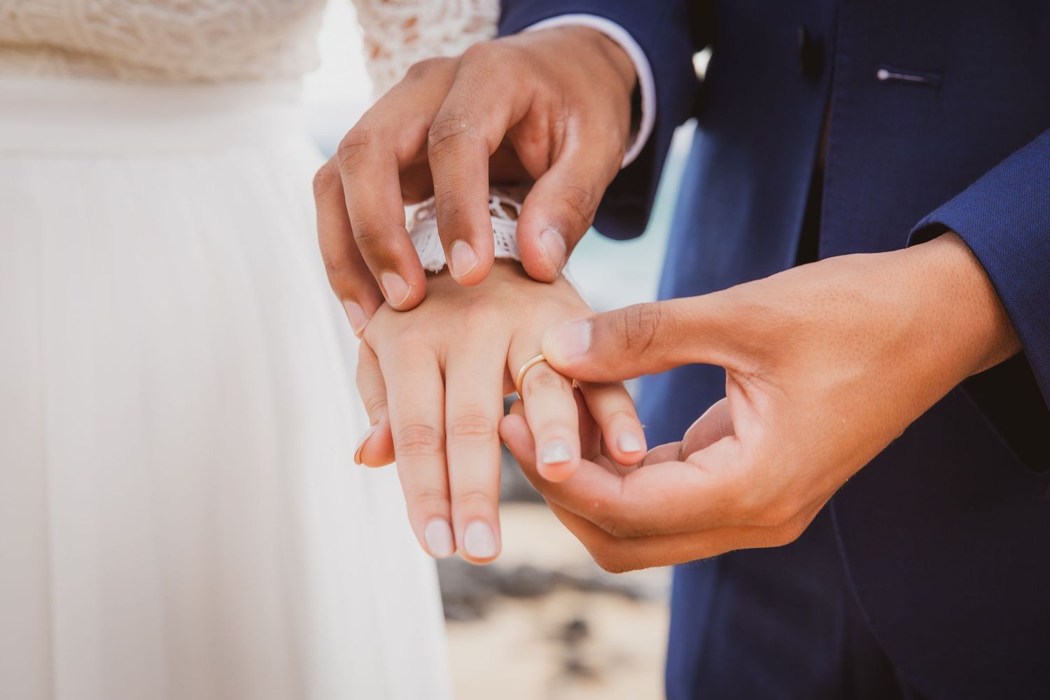 Couple exchanging wedding rings during marriage ceremony, groom placing gold band on bride's finger.