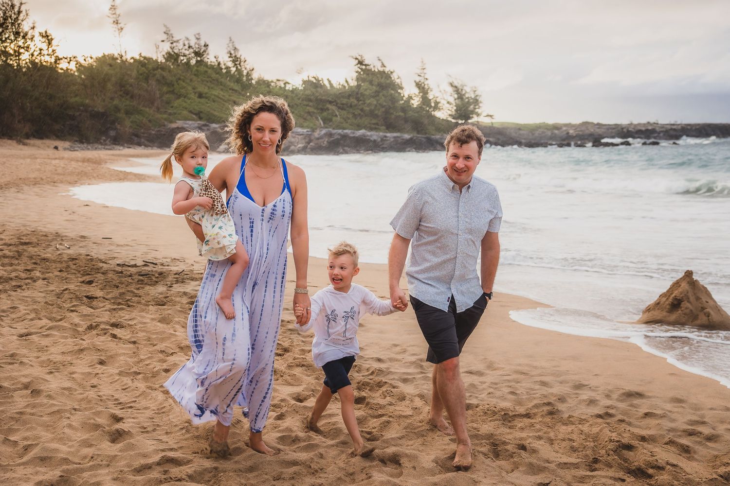 Family walking together along a beautiful beach shoreline in coordinated blue and white outfits.