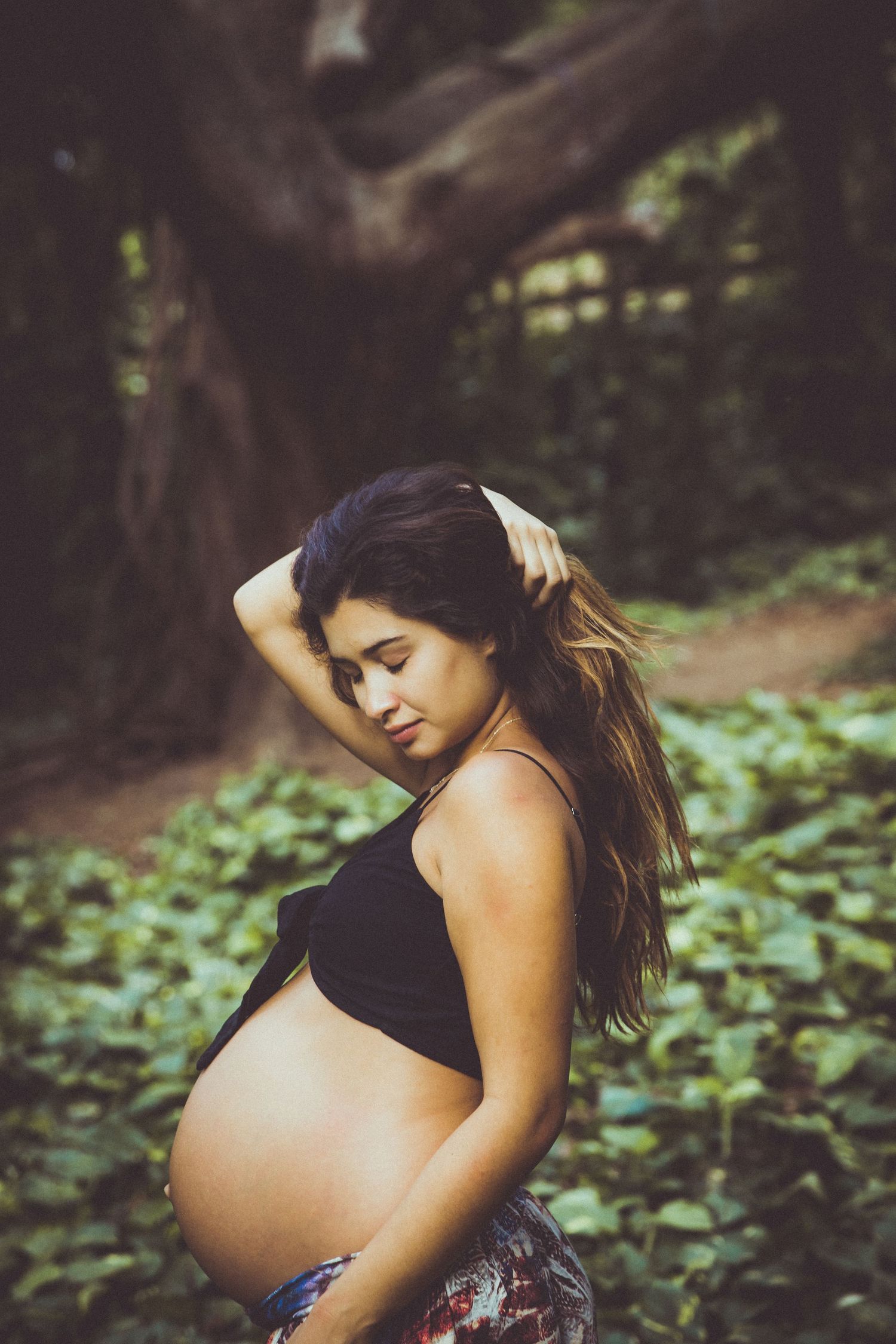 Intimate maternity portrait captured in a forest setting with soft natural lighting.