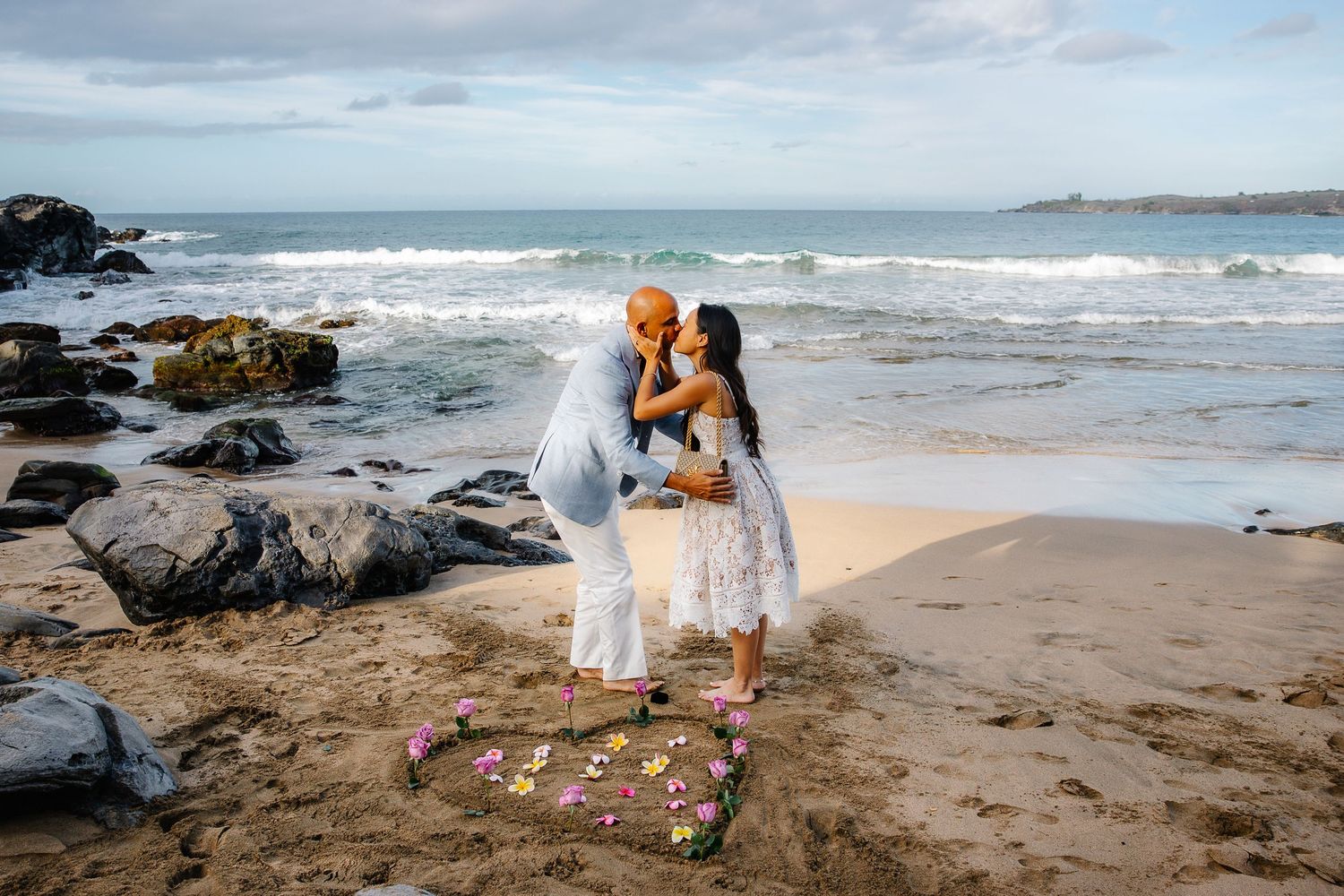 Scenic beach proposal setup with scattered roses and volcanic rocks.