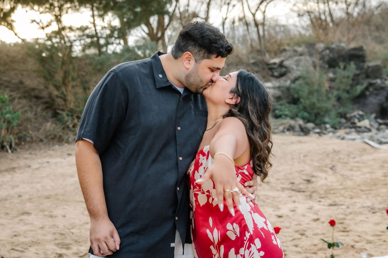 A tender moment captured on a scenic beach with rocky cliffs in the background.