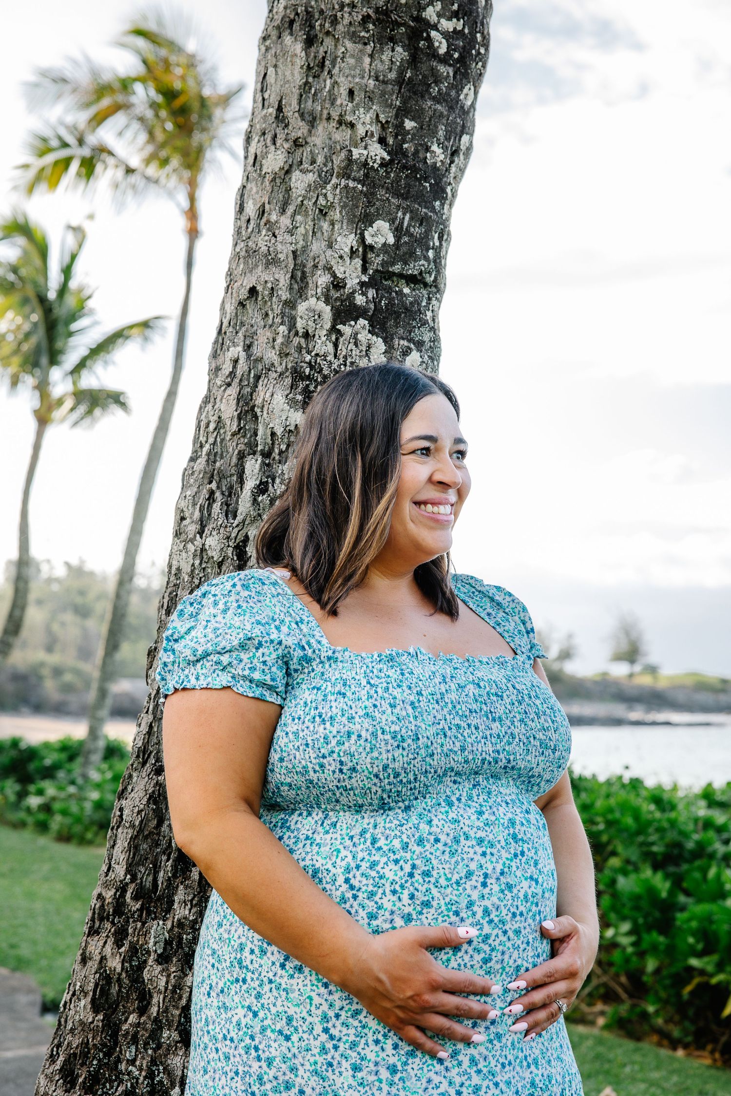 A woman in a blue floral dress poses in front of palm trees on a sunny day.
