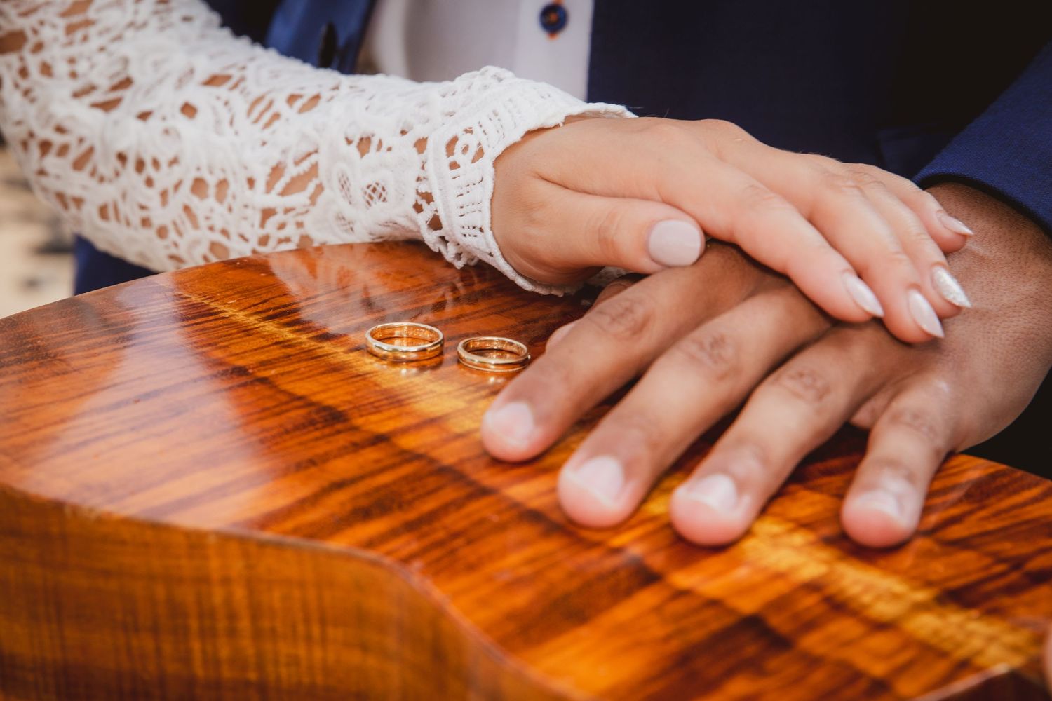 Newlywed couple placing gold wedding rings on a wooden surface, hands gently touching in a romantic ceremony moment.