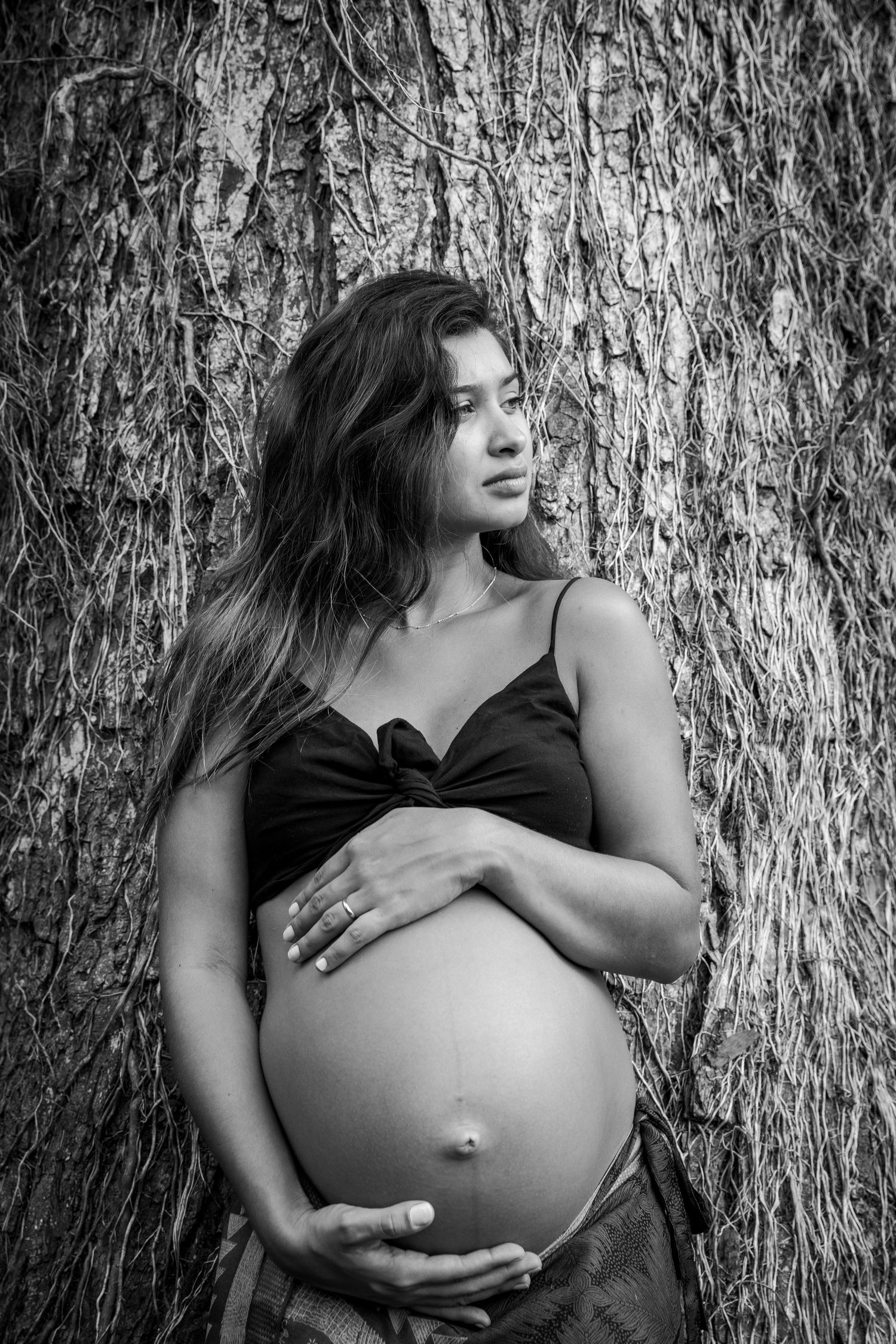 Black and white maternity portrait against a textured tree bark backdrop.
