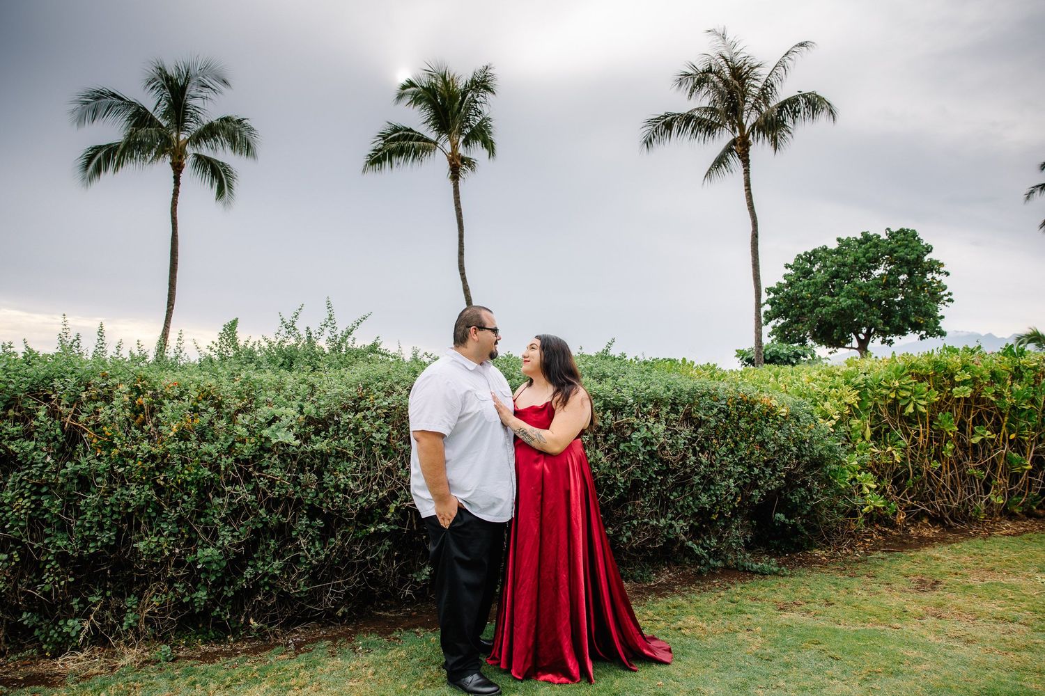 Couple's portrait session among palm trees and tropical landscaping near the ocean.