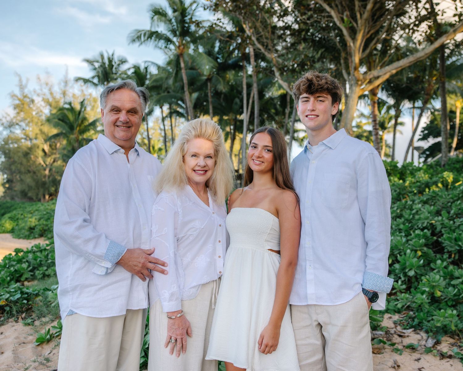 A family portrait on a tropical beach with palm trees and lush greenery.