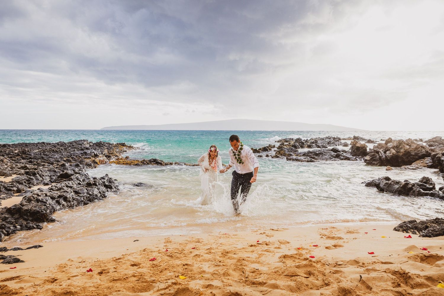 Panoramic beach scene with turquoise waters, volcanic rocks, and sandy shoreline.