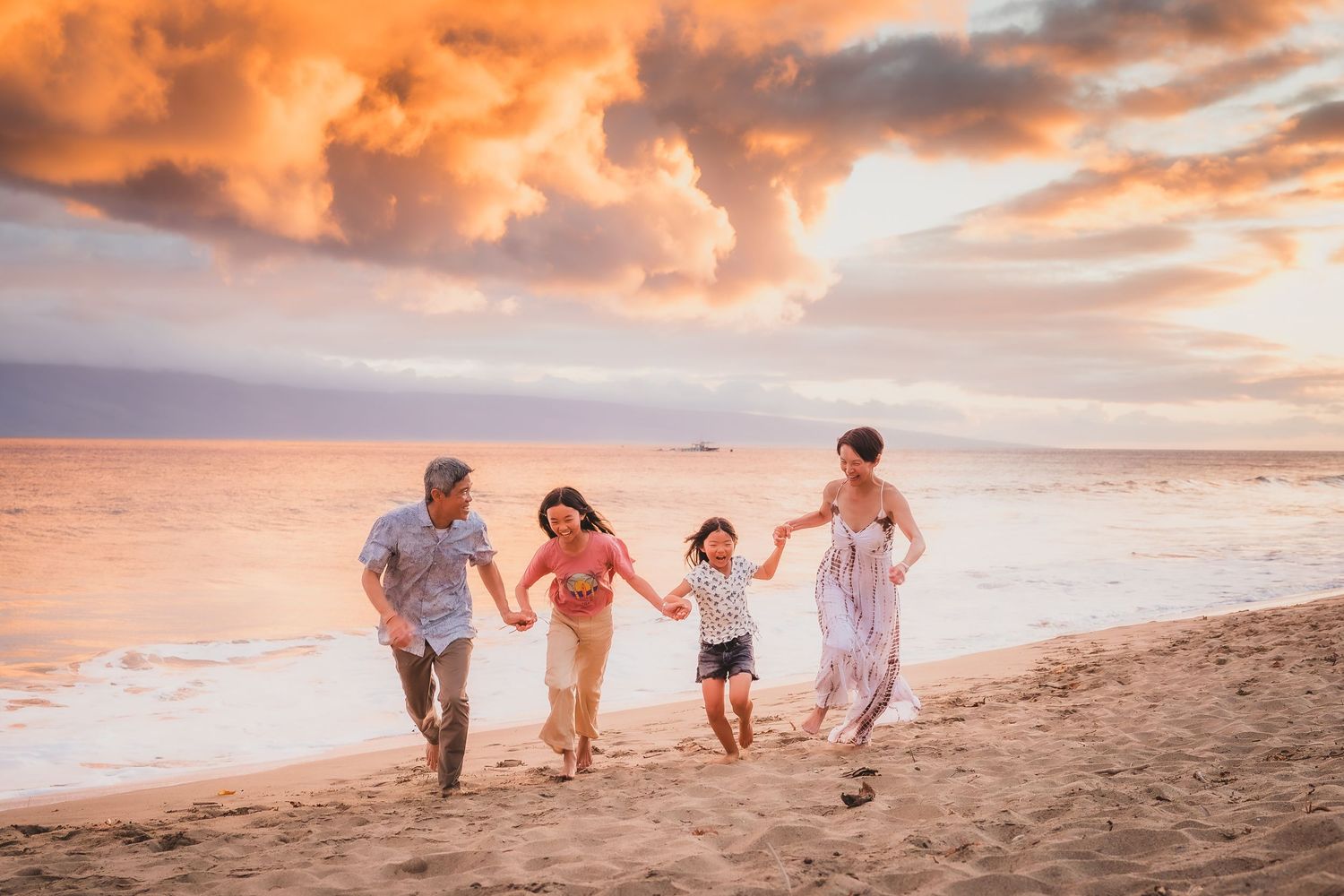 Family of four joyfully running on a sandy beach at sunset with dramatic orange clouds over the ocean.