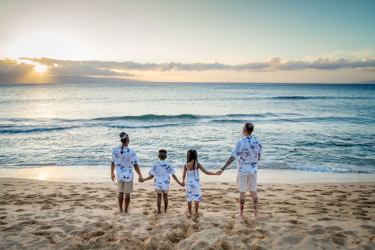 Silhouettes of people walking together on sandy beach at sunset with ocean waves and golden sky in background.