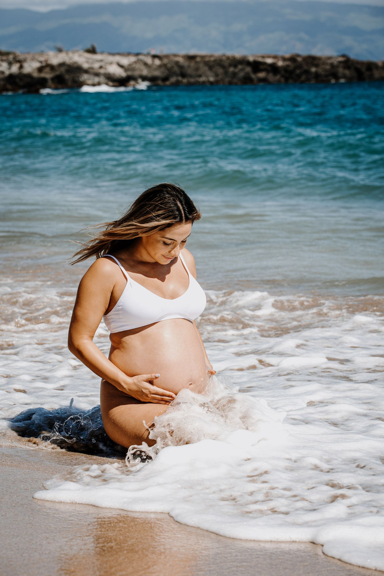 A peaceful maternity moment captured with ocean waves washing over the sandy beach.