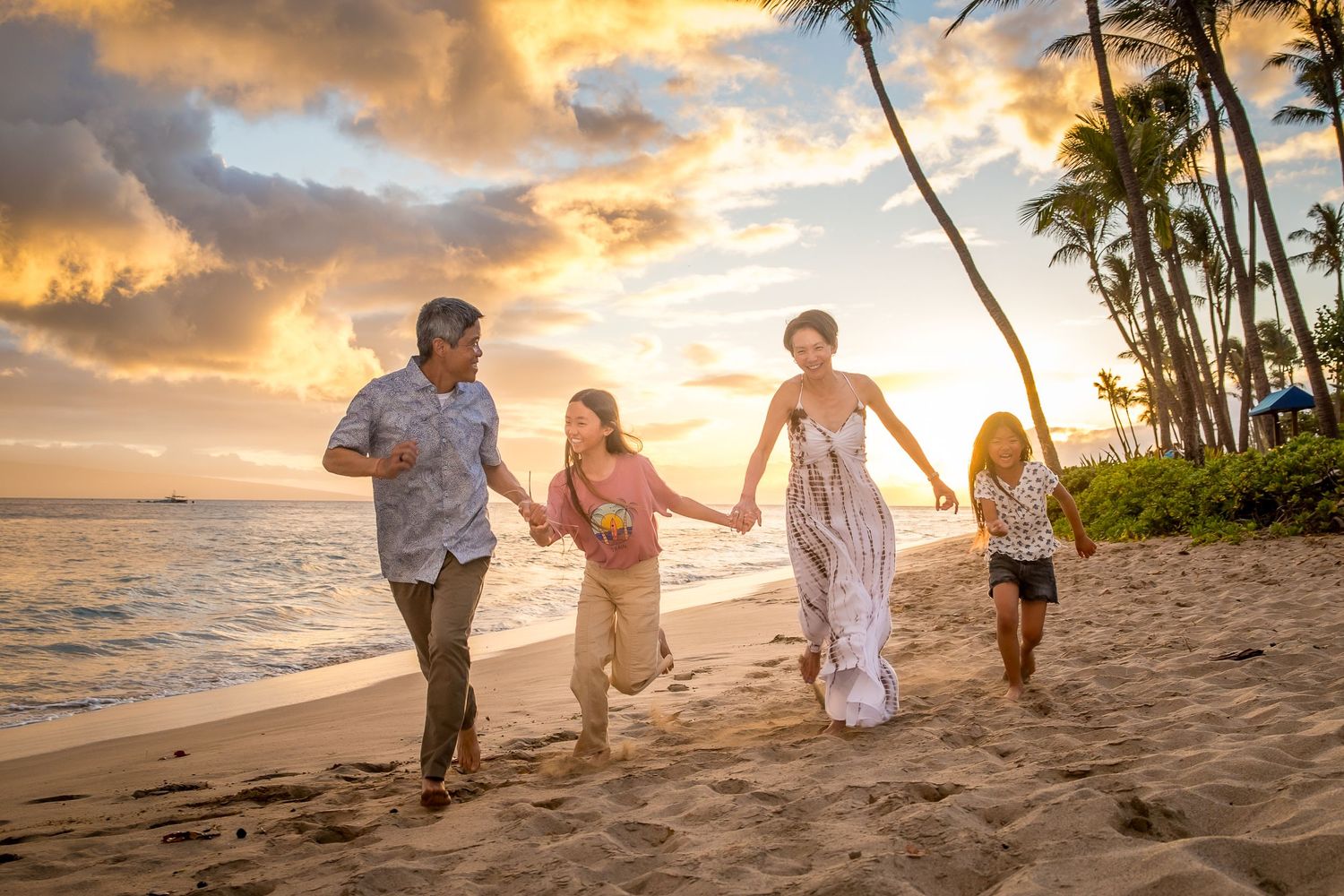 Family walking along tropical beach at golden sunset with palm trees silhouetted against sky.