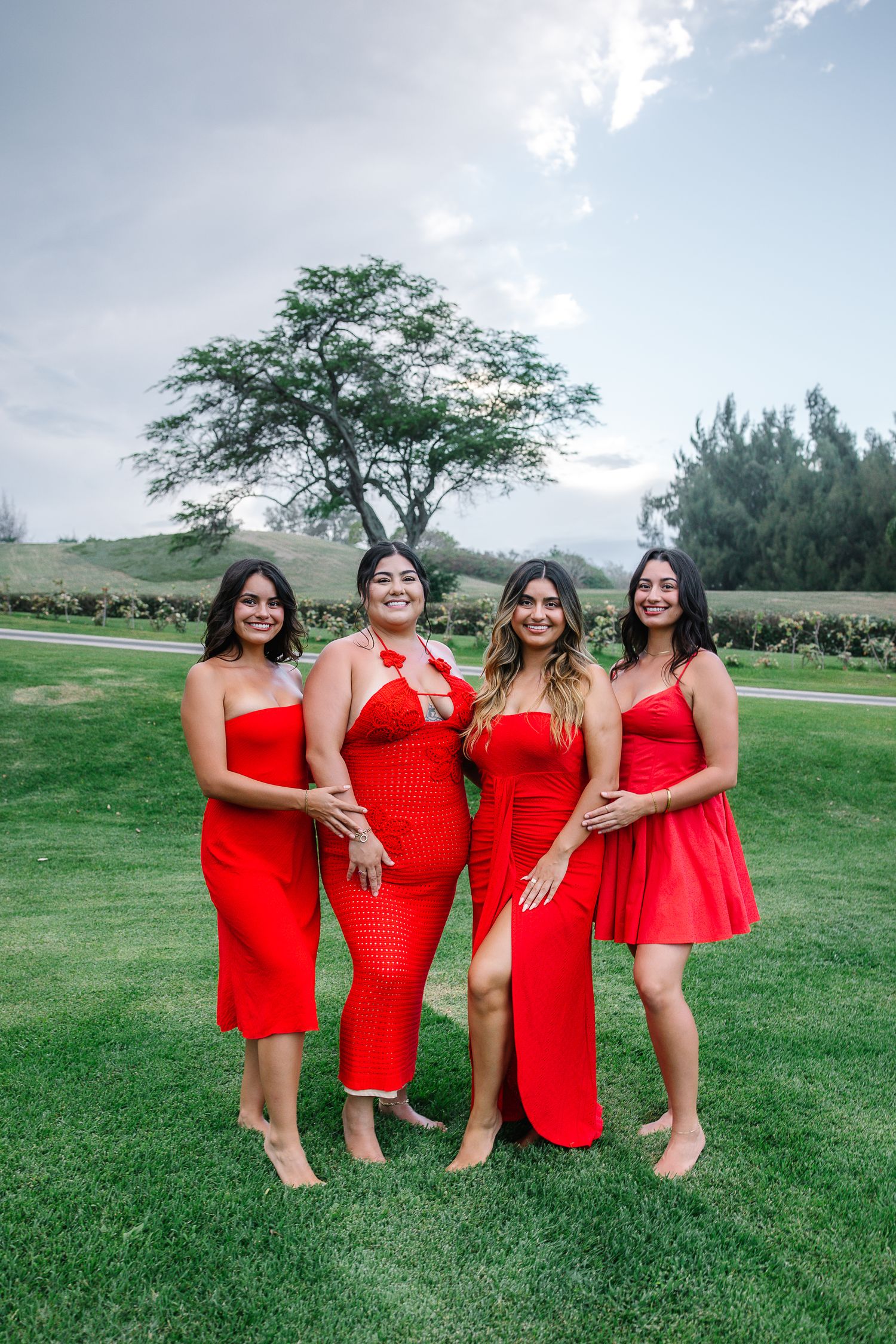 Bridesmaids in matching red dresses pose playfully on a green golf course.