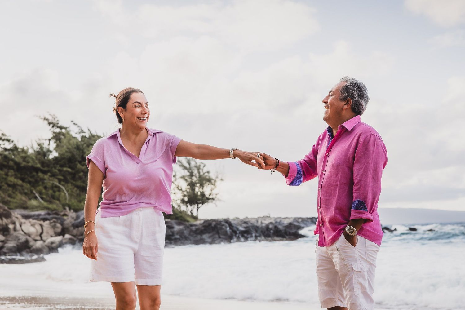 Family members holding hands and walking along a scenic beach path in pink and white outfits.