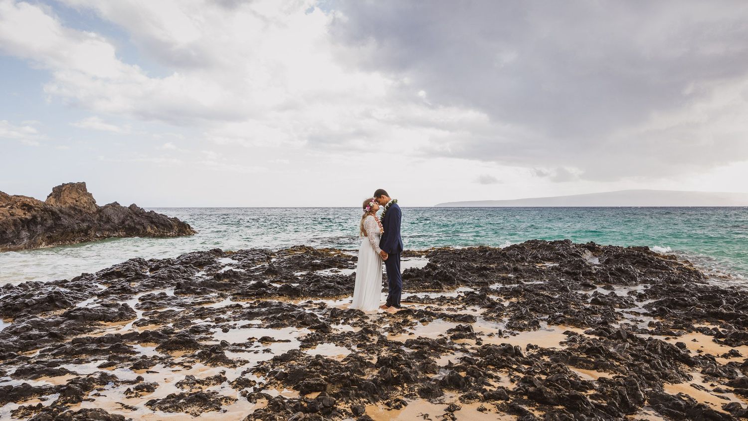 Panoramic view of a Hawaiian beach with dramatic clouds and volcanic rock formations.