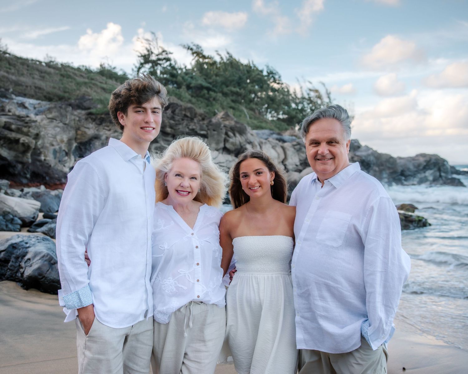 Casual family beach portraits with rocky coastline and ocean waves in background.