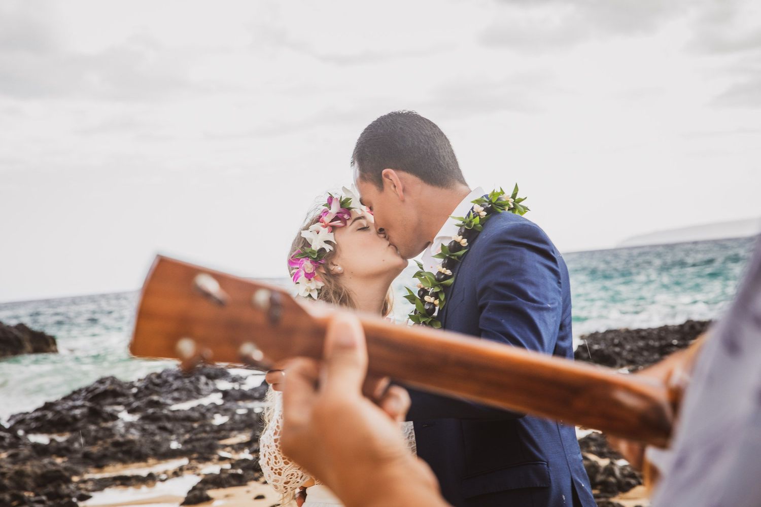 A romantic beach wedding moment with ukulele music and traditional Hawaiian leis.
