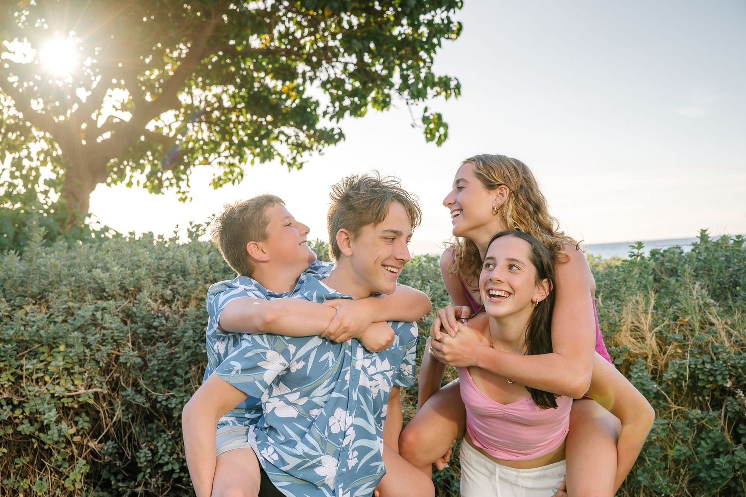 Candid family photo session showing joyful interactions outdoors at sunset with greenery in background.