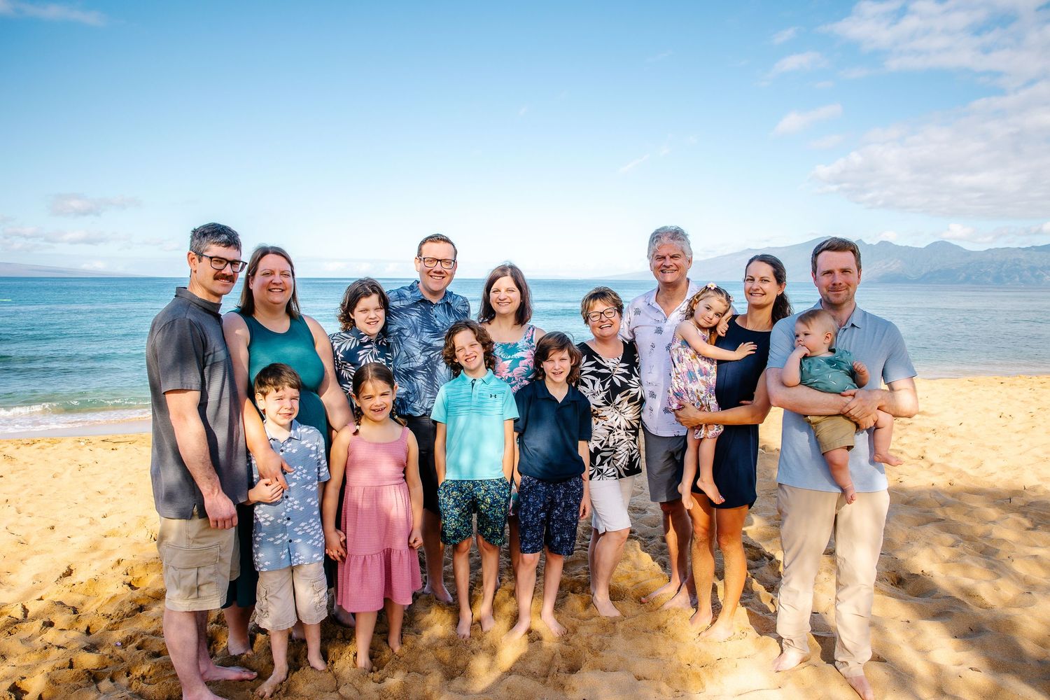A group of people posing together on a scenic beach with blue ocean and mountains in the background.