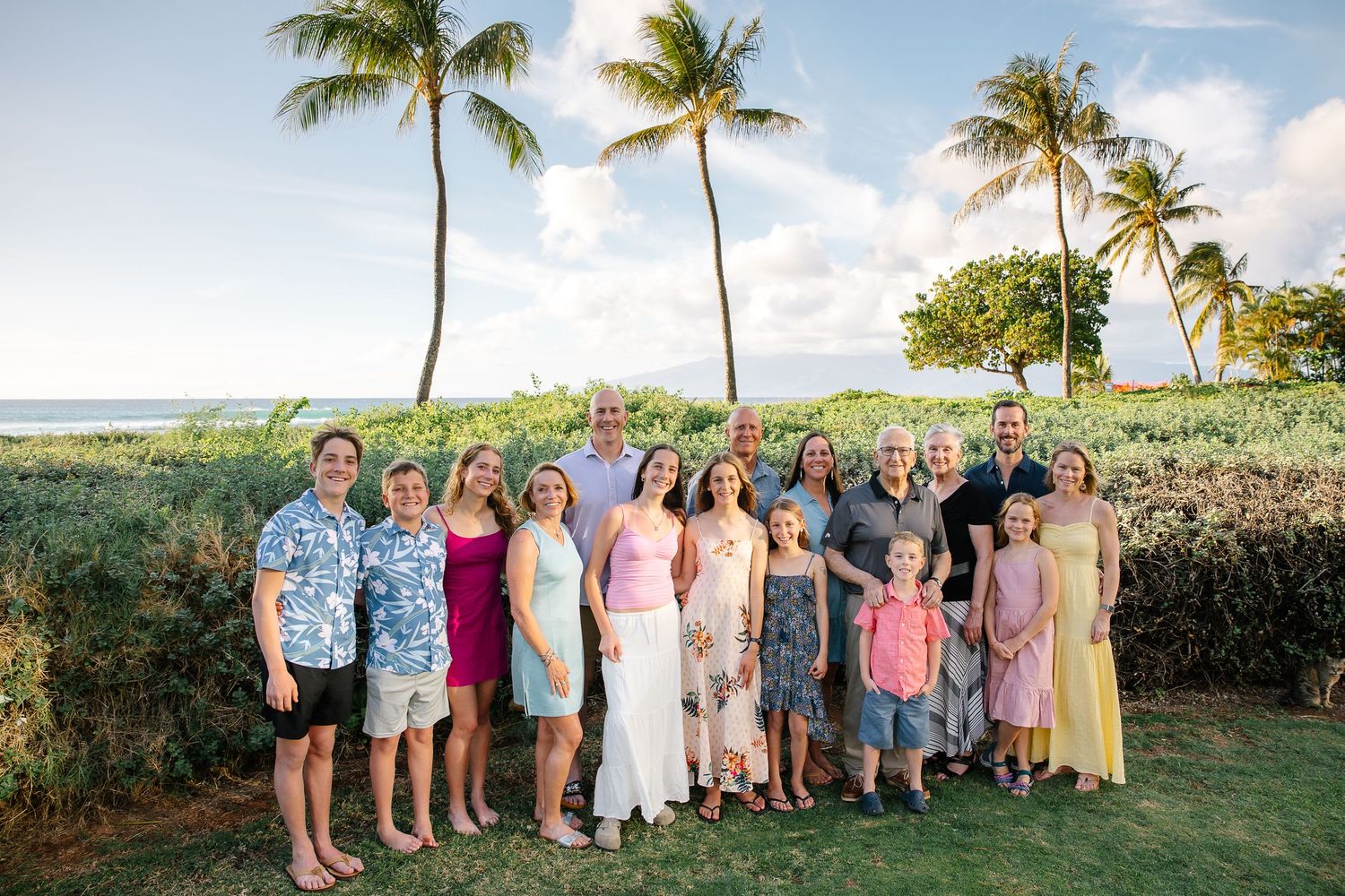 Large family group photo with everyone wearing coordinated pink and blue outfits by palm trees.