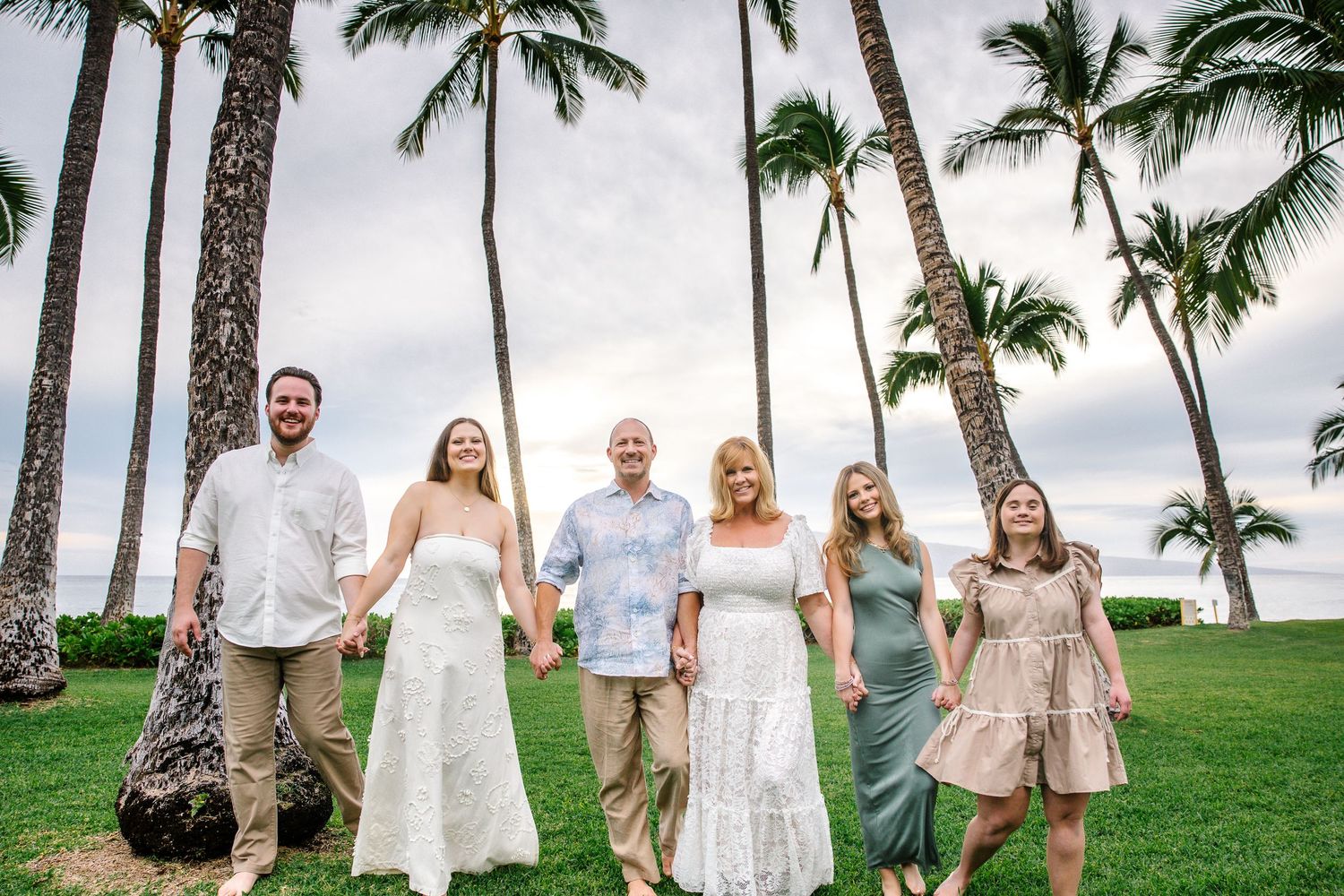 Family members pose playfully on a palm-lined lawn near the beach in tropical Hawaii.
