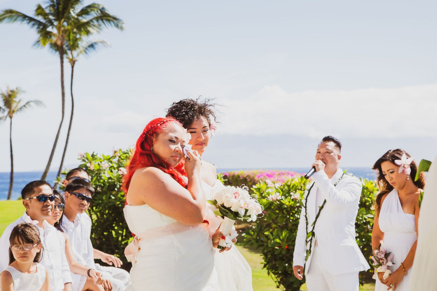 Bride and groom embrace joyfully at outdoor Hawaii wedding ceremony with palm trees and ocean backdrop.