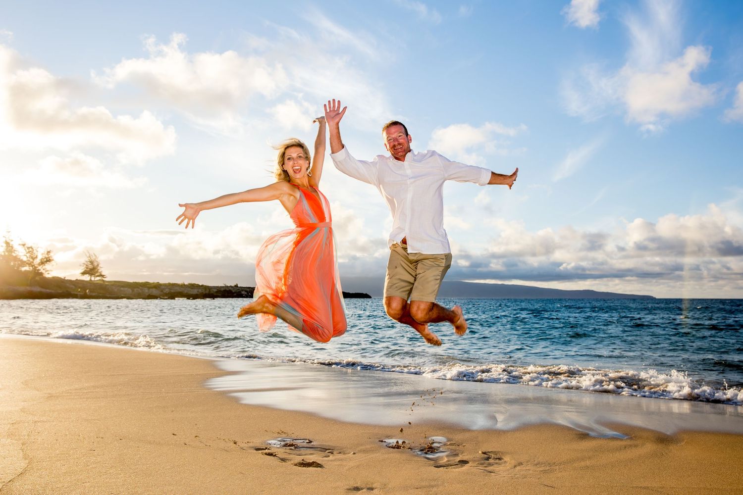 Playful couple in white and orange outfits enjoying a sunny day at the beach.