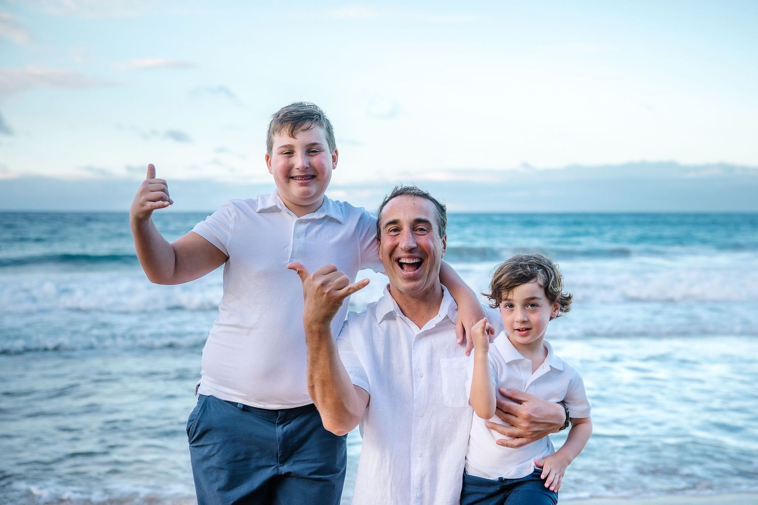 Three people celebrating and laughing together on a beach at sunset.