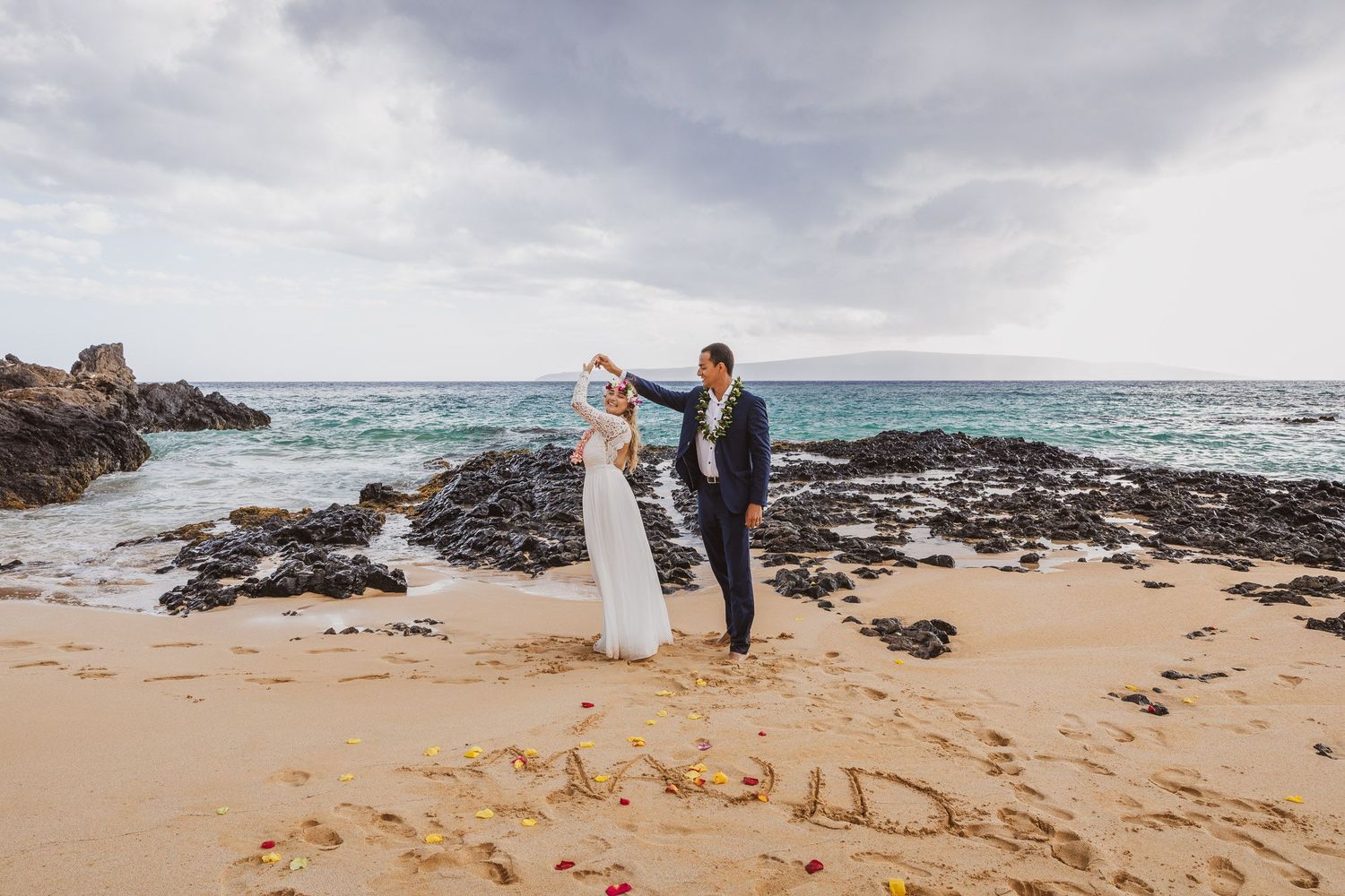A romantic dance on the beach with waves crashing against volcanic rocks.