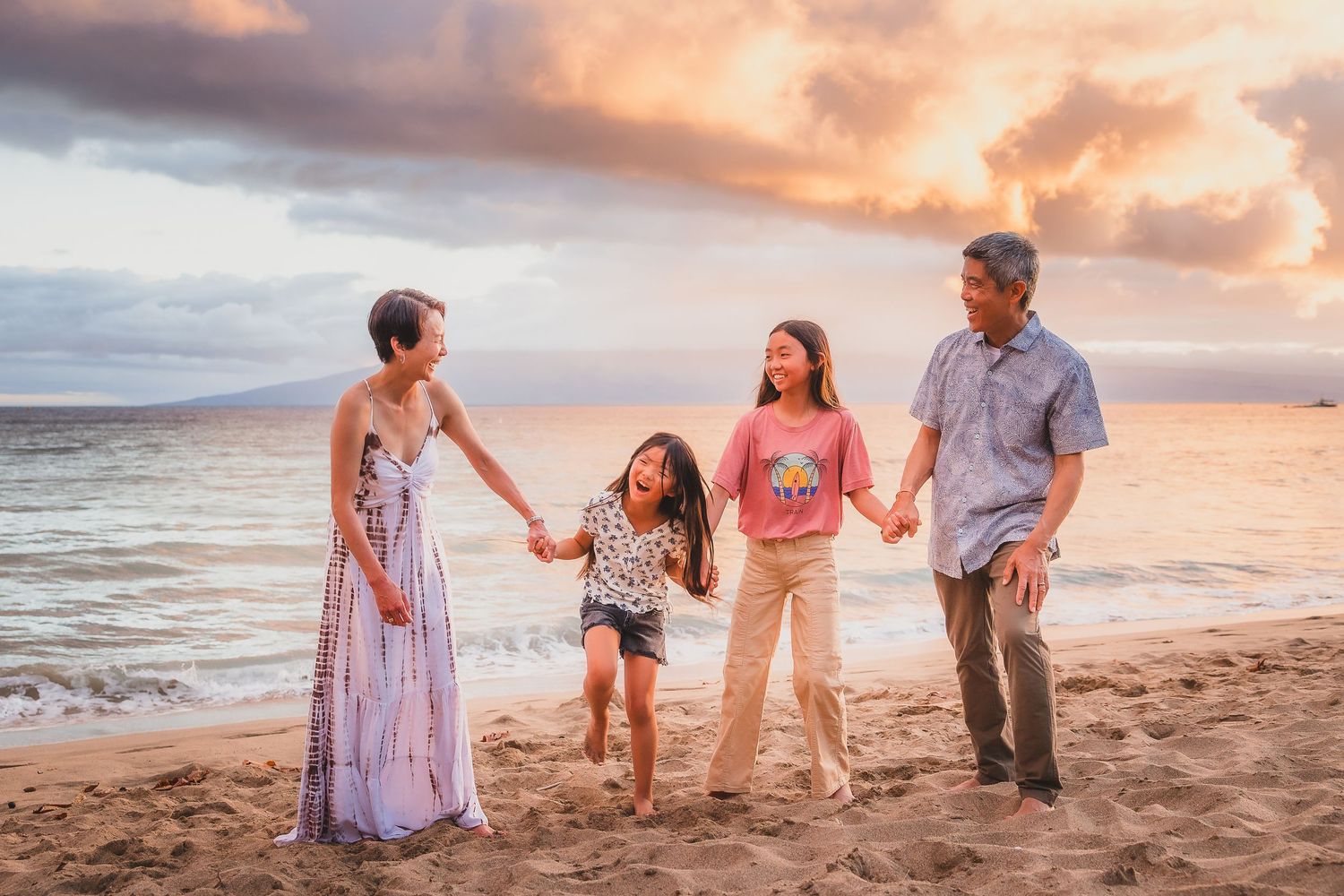 Family playing together on beach at sunset with ocean waves in background.