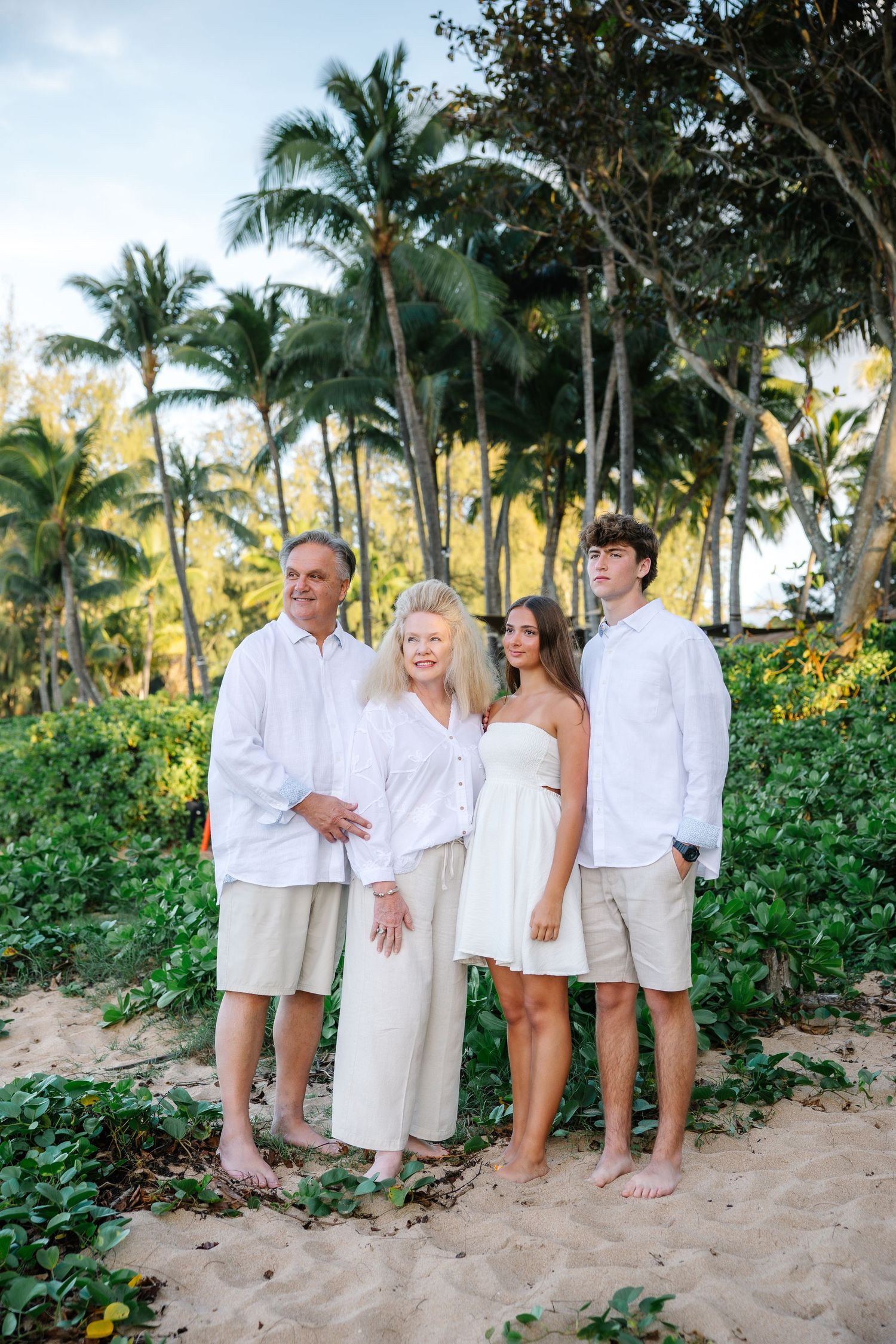 Beach family photos with palm trees and ocean backdrop, everyone dressed in white and beige.