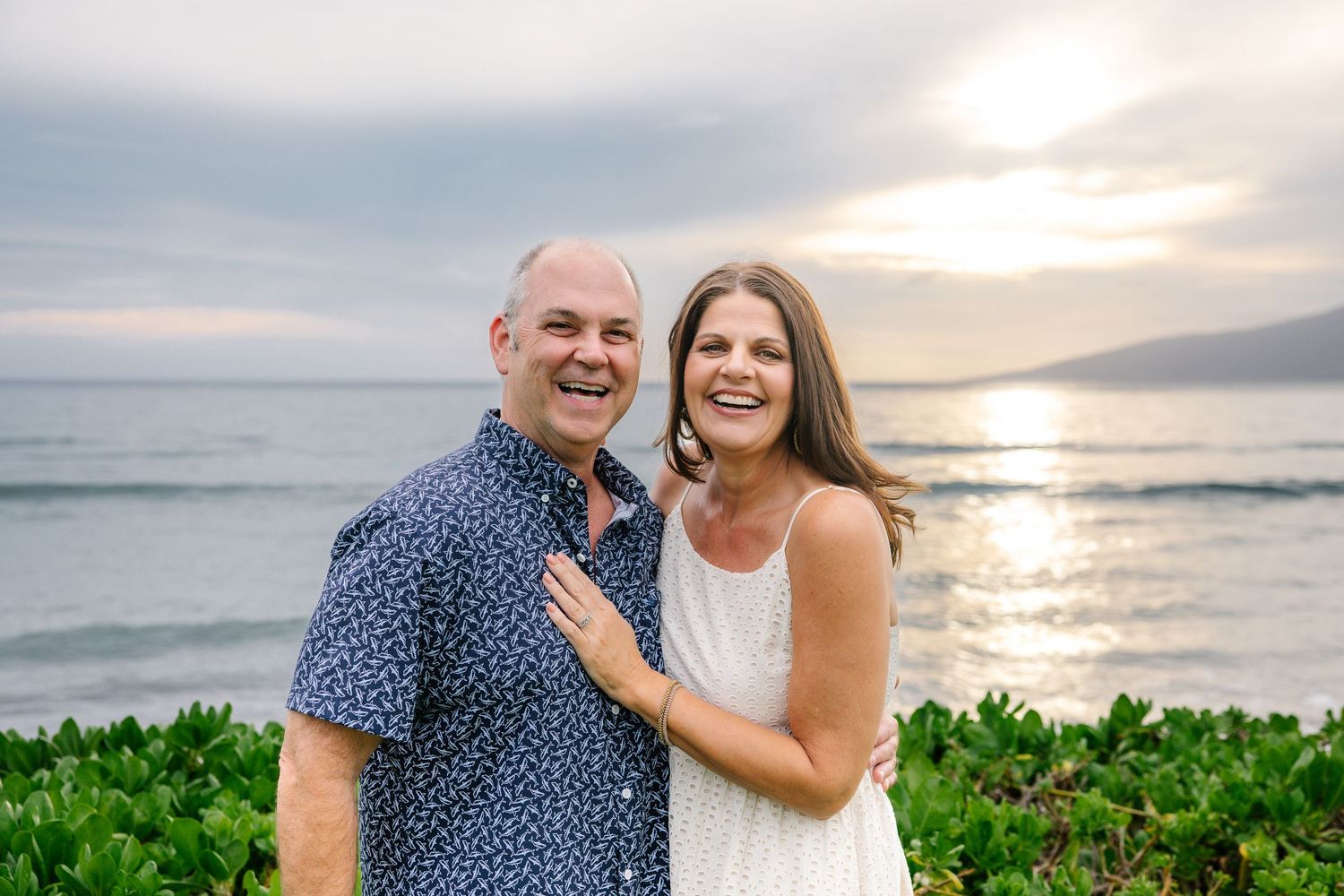 A couple shares an intimate moment on a Hawaiian beach during golden hour with ocean views.